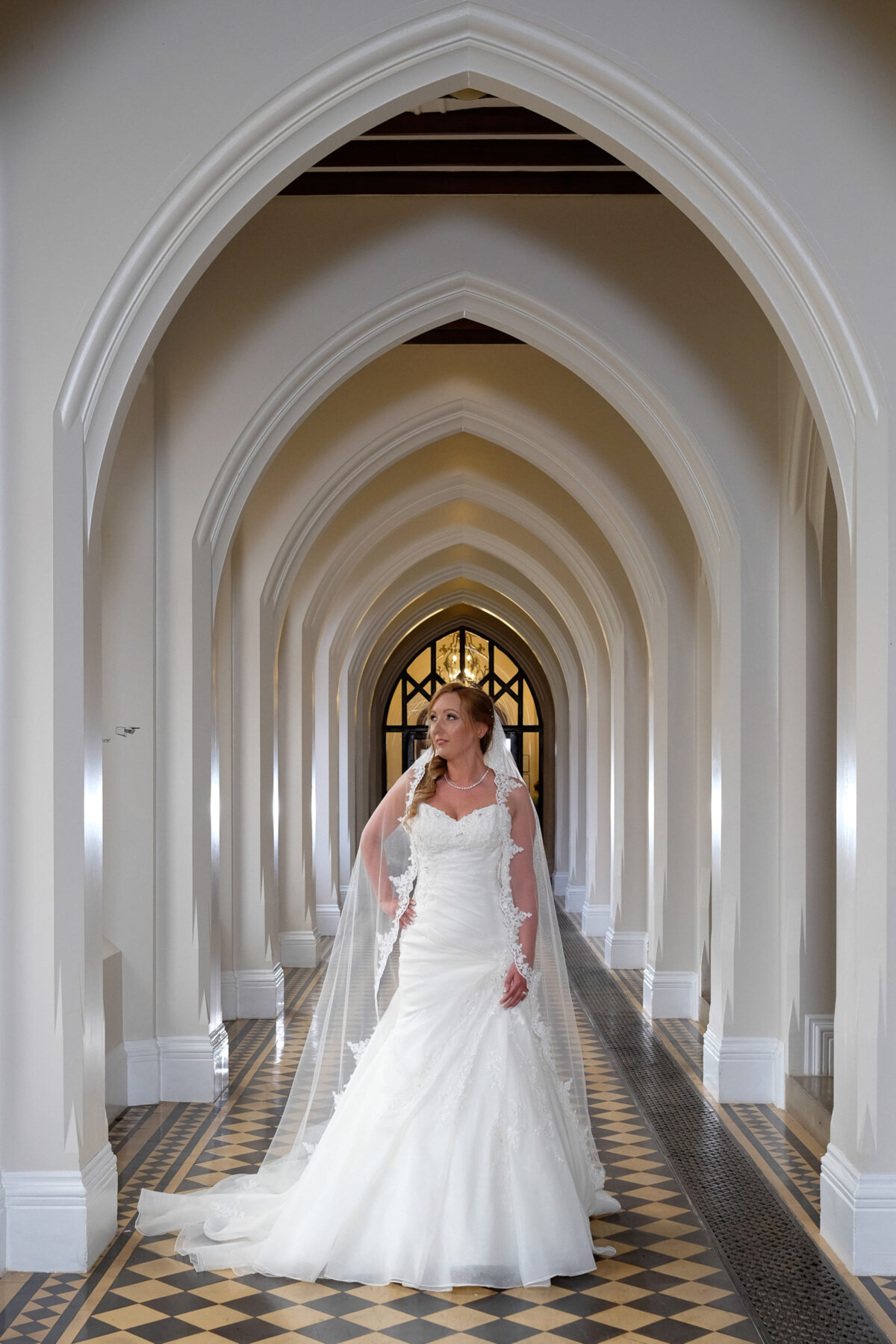 "Bride walking through arched corridor at Stanbrook Abbey"
